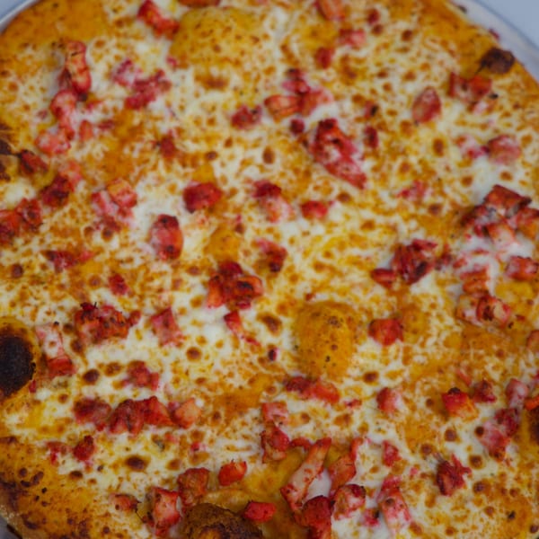 Close-up of a Moon Pizza with melted cheese and red chicken tikka pieces.