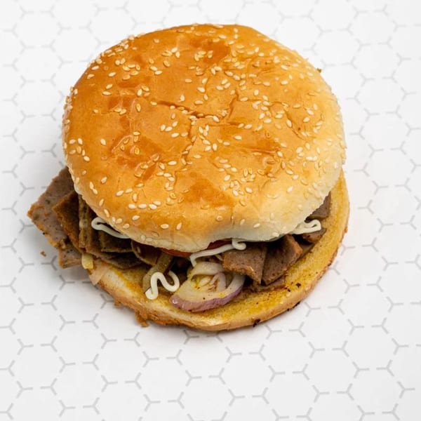 A Moon Pizza gyro sandwich with sliced meat, onions, and white sauce on a sesame seed bun.