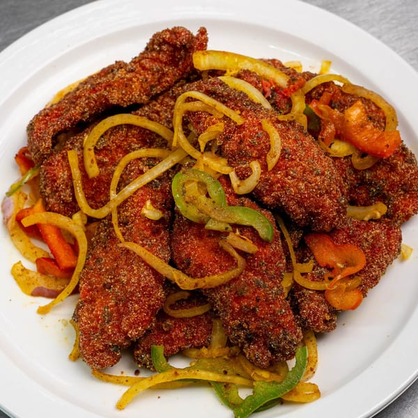 Crispy fried chicken strips seasoned with spices, served with sautéed onions and bell peppers on a white plate.