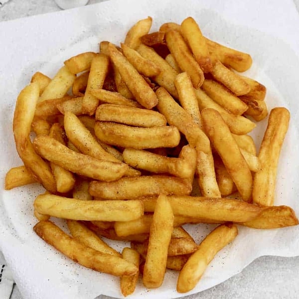 Golden-brown, seasoned french fries piled high on a white paper-lined plate.