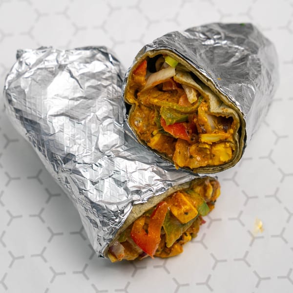 Two foil-wrapped burritos, cut in half, revealing a filling of paneer, peppers, and onions.