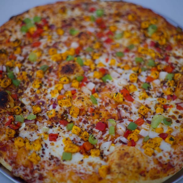 Moon Pizza's paneer pizza, topped with cheese, red and green peppers, onions, and chili flakes.