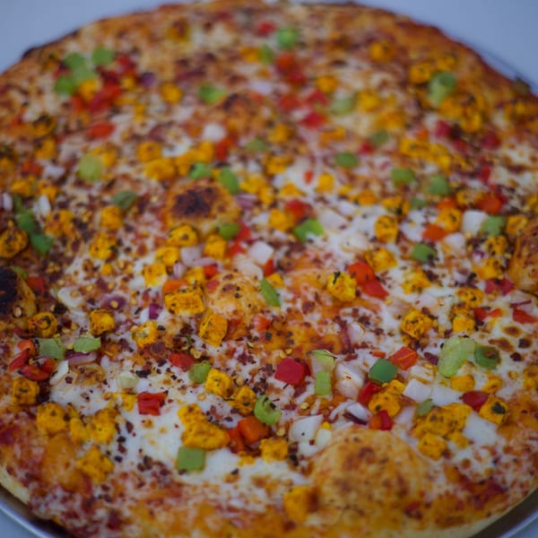 Close-up of a Moon Pizza with paneer, red and green bell peppers, and onions.