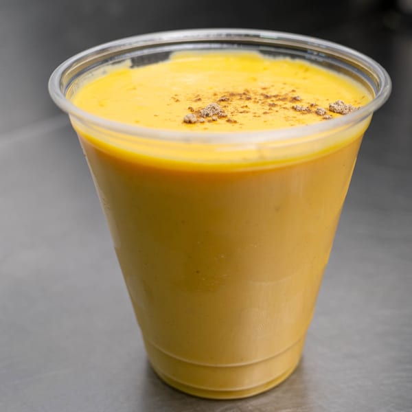 A plastic cup filled with a golden-yellow beverage, topped with a sprinkle of dark spices.