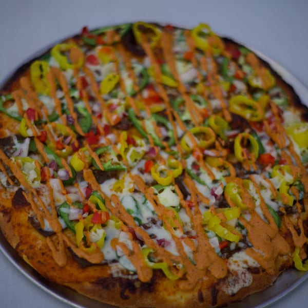 Moon Pizza's specialty pizza with green and yellow peppers, red onions, and a spicy orange drizzle.