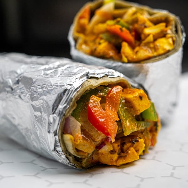 Two foil-wrapped burritos filled with chicken, red and green peppers, and onions.