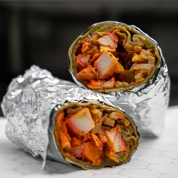 Two foil-wrapped burritos, cut in half, revealing chicken and vegetables inside.