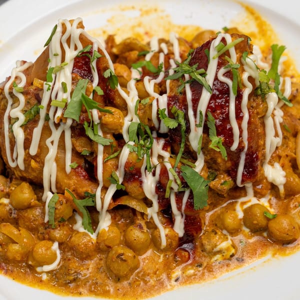 Close-up of chicken and chickpeas in a rich sauce, drizzled with white cream and garnished with herbs.