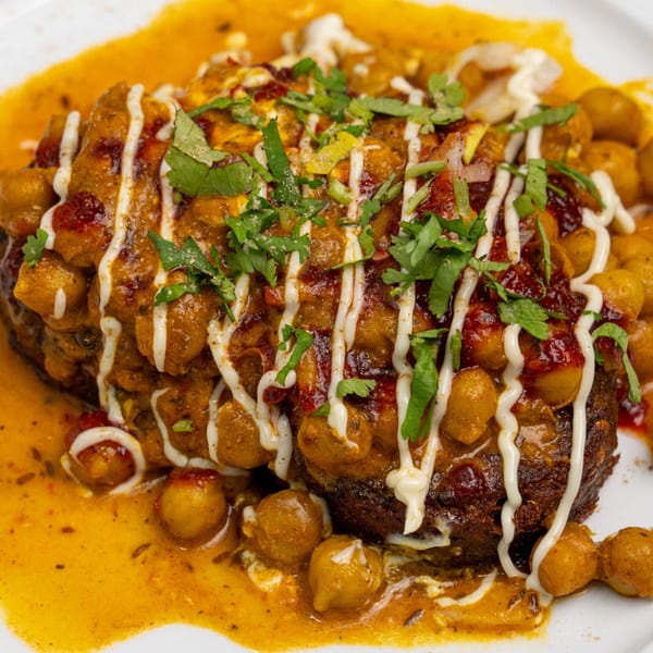 A close-up of a savory dish with chickpeas, a rich sauce, white drizzle, and fresh cilantro.